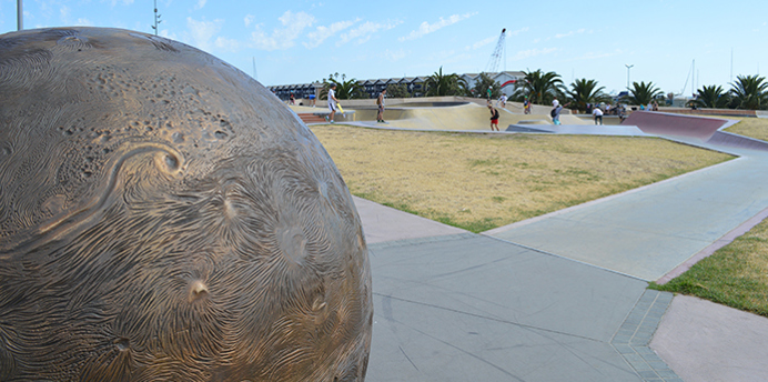 Skaters using the Marina Skate Park with the boat sheds in the background. Wide paved footpaths provide easy access.  
