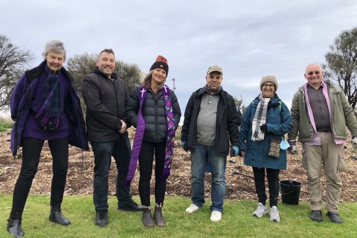 A group of people stand in a park in front of recently planted trees 